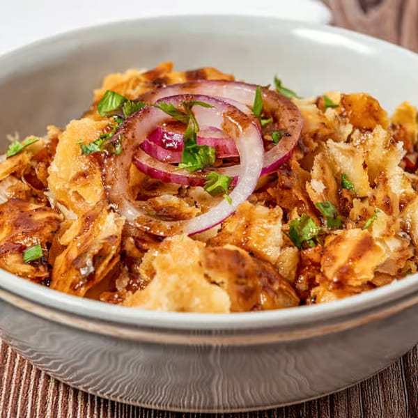 Close-up of a Pakistani street food snack with crispy fried dough, red onions, and sauce in a bowl.