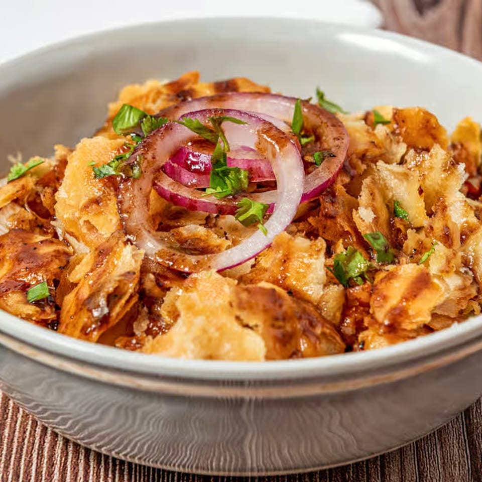 Close-up of a Pakistani street food snack with crispy fried dough, red onions, and sauce in a bowl.