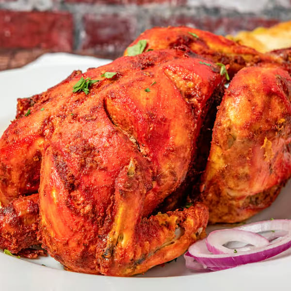 Whole roasted chicken, bright red from spices, garnished with cilantro and red onion slices.